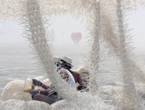 Third Space spatial installation made of white woven cable ties with wild spiky structure emerges pillows, columns and nets on which sits a person wearing a straw hat