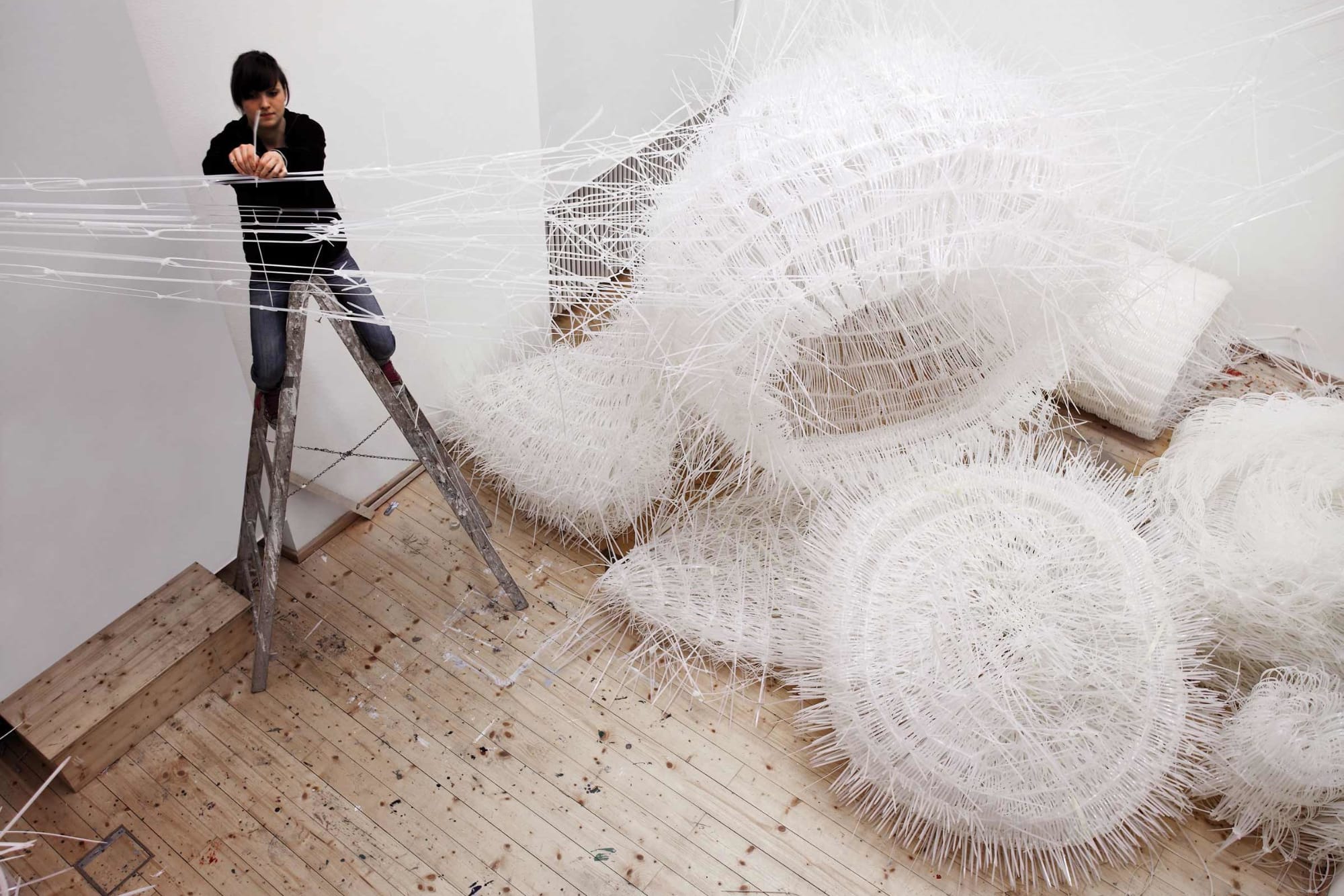 Third Space spatial installation of white woven cable ties with wild spiky structure creates caves, columns and nets. Person on a ladder securing cable ties.