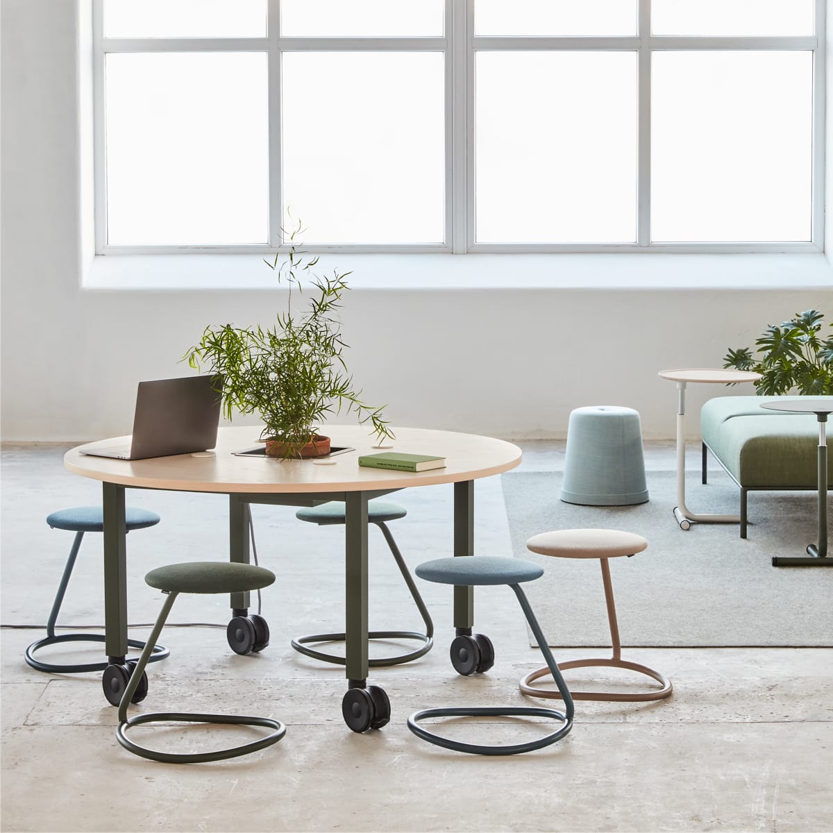 Rocca stool with bent steel tube ring for ergonomic rocking that acts as a support leg and seat cushion in different colors at a round table in large industrial hall