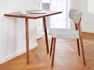 Marlon Dining Chair with wide back and seat in modern dynamic shape covered with light fabric and light wood legs with plain table