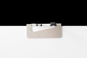 Cable Clip made of bent and punched metal holds various cables on white desk with dark background