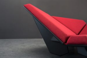 Cay Sofa with different geometric cushions turned in different directions and covered with red fabric and a dark frame