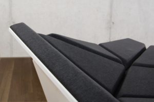 Cay Sofa with different geometric cushions turned in different directions and covered with dark grey fabric and a white geometric frame