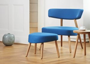 Marlon Lounge Chair with wide back and seat in modern dynamic shape covered with light blue fabric and light wooden legs with chair for footrest and side table with coffee cup