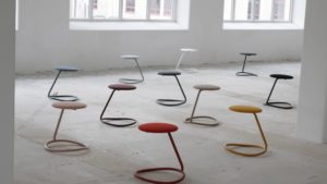 Rocca stool with bent steel tube ring for ergonomic rocking that acts as a support leg and seat cushion in different colors in large industrial hall