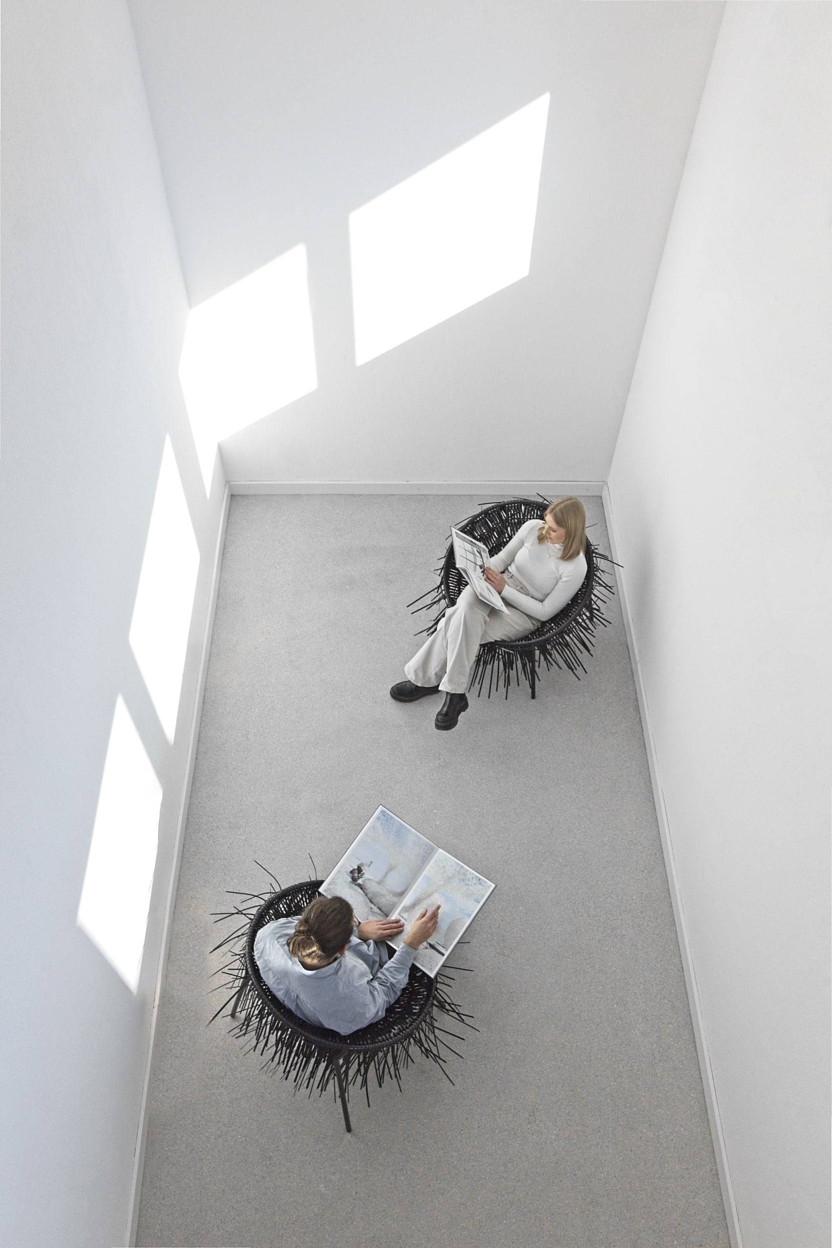 Zwei Personen sitzen auf Oricio-Sesseln aus verflochtenen Kabelbindern in einem hellen Raum