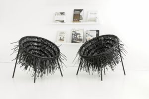 Two Oricio armchairs made of interwoven zip ties with wild spiky structure in light room with bookshelf in background