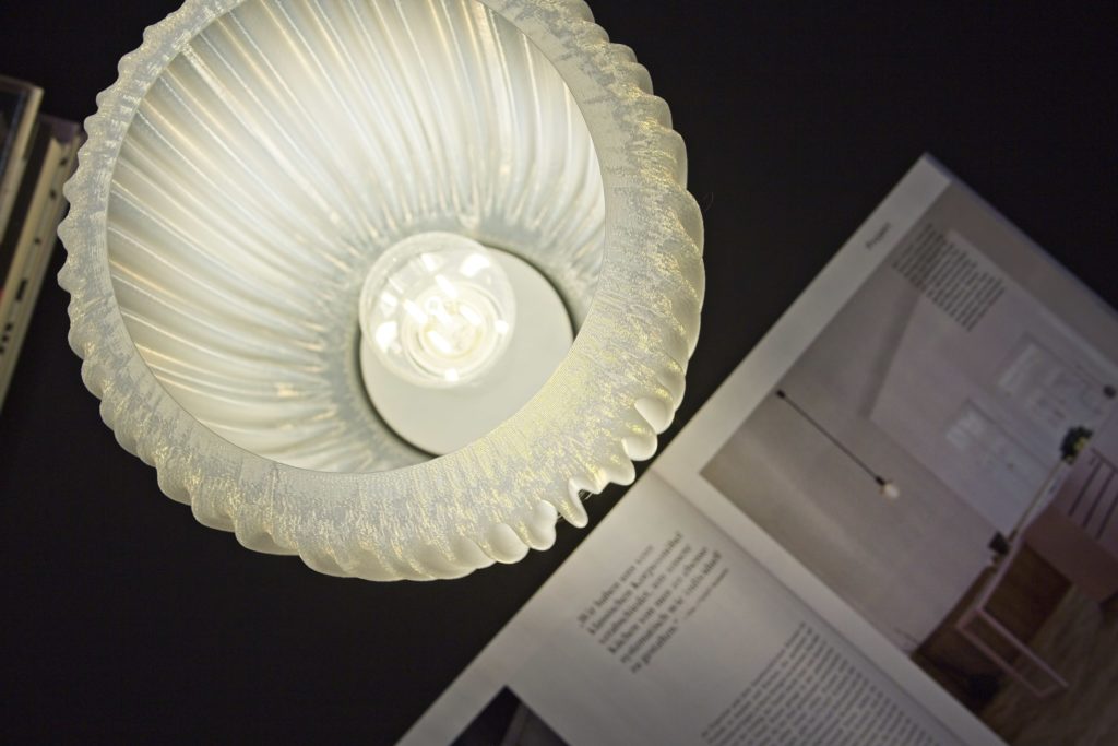 Table lamp with organically folded lampshade and light bulb and magazine in dark environment